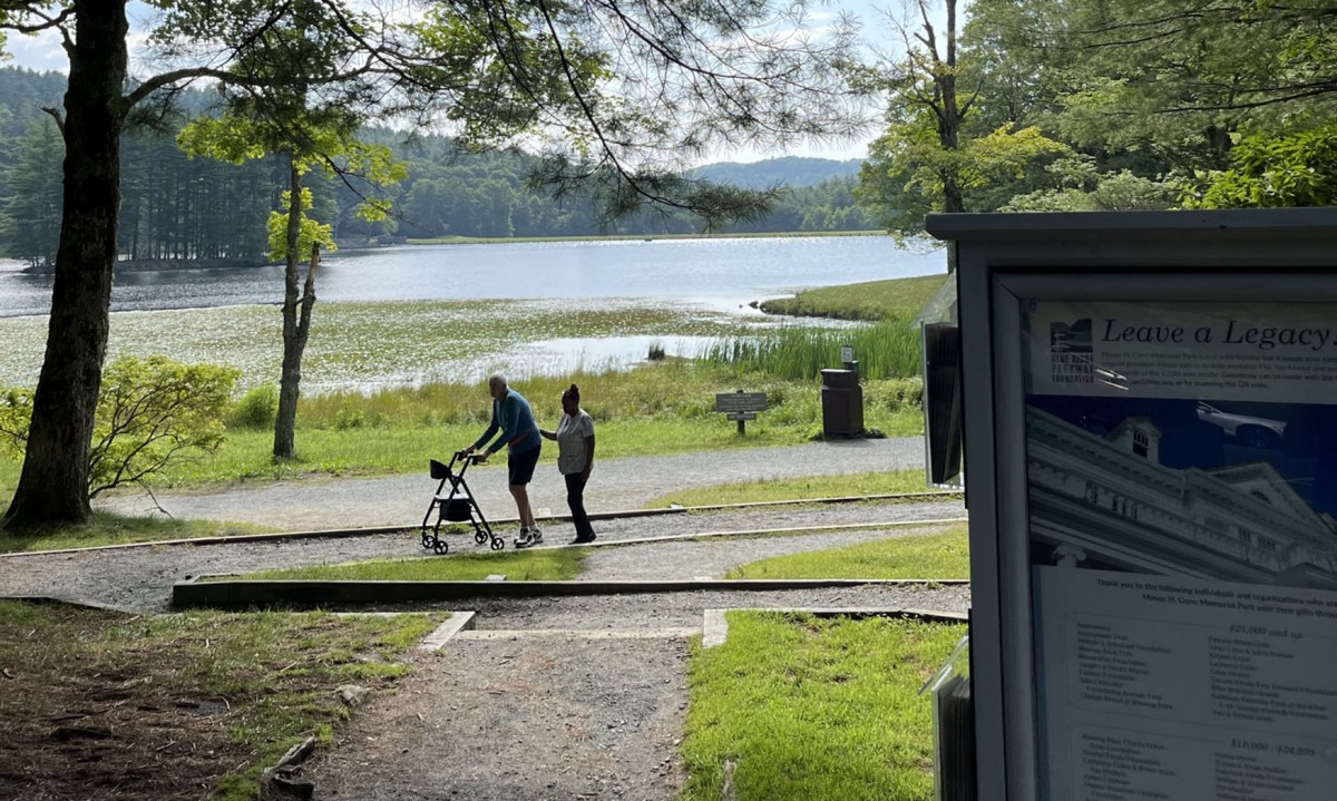 A man using a walker is assisted up the gravel ramp at Bass Lake