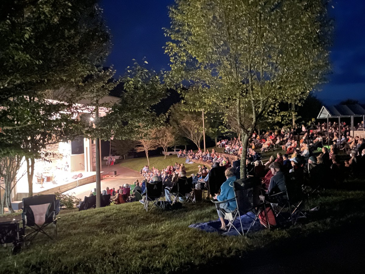 Crowd sits in amphitheater looking at lighted stage at night at Blue Ridge Music Center